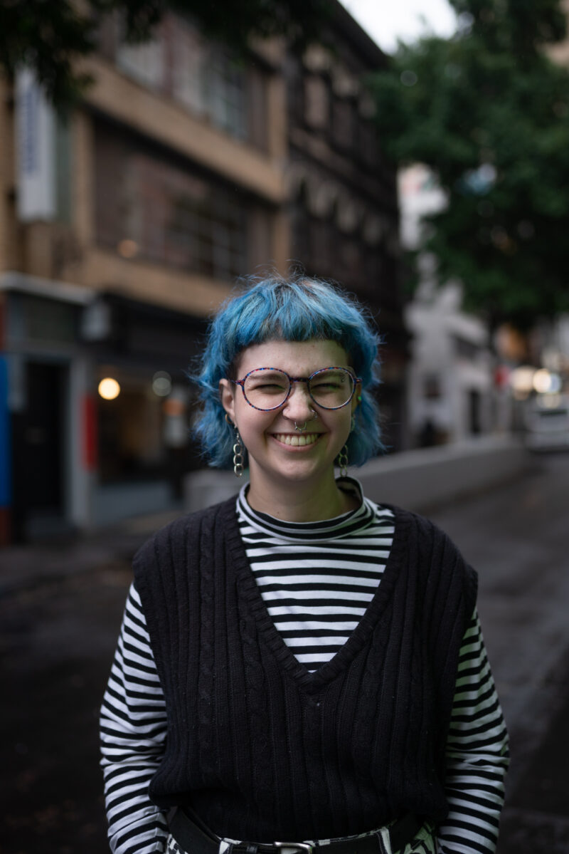 Is Hay (they/them) is facing the camera, smiling with her nose and eyes scrunched up.