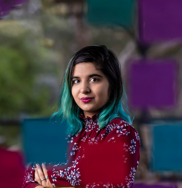 Young woman with black and green hair looking at the camera with her arms crossed in front of her in a strong pose.
