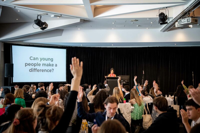 Image of young people with their hands up at the SA SRC Summit 2022. There is a sign in the back that reads: Can young people make a difference