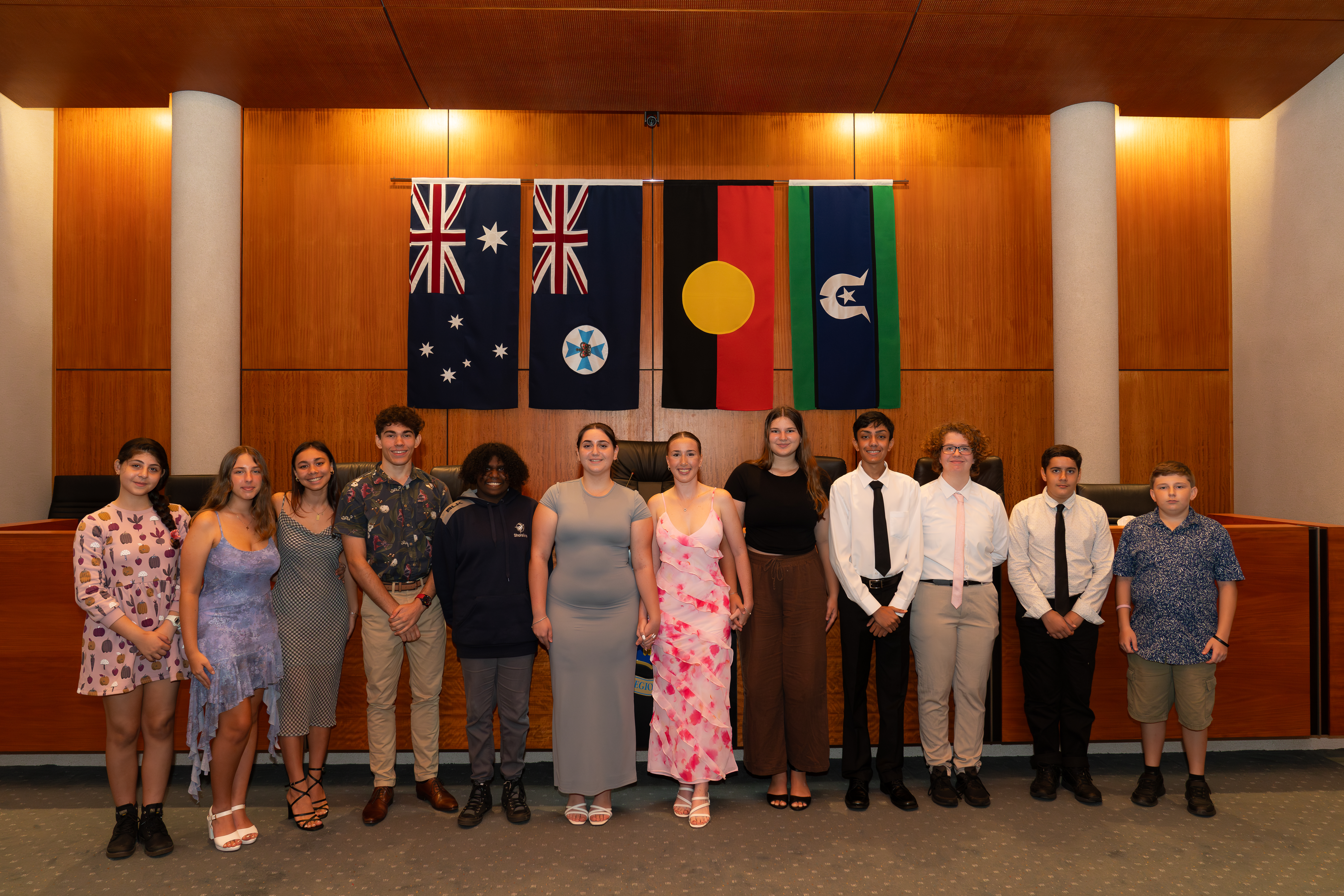 Ten young people stand side by side inside the Cairns Council Chamber rooms. 